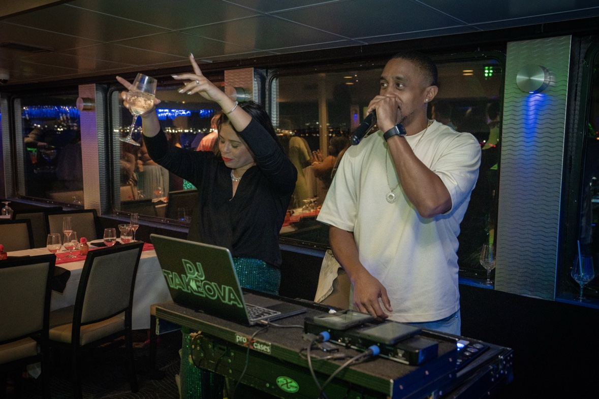 DJ Takeova speaking on the microphone at his DJ booth during a boat party