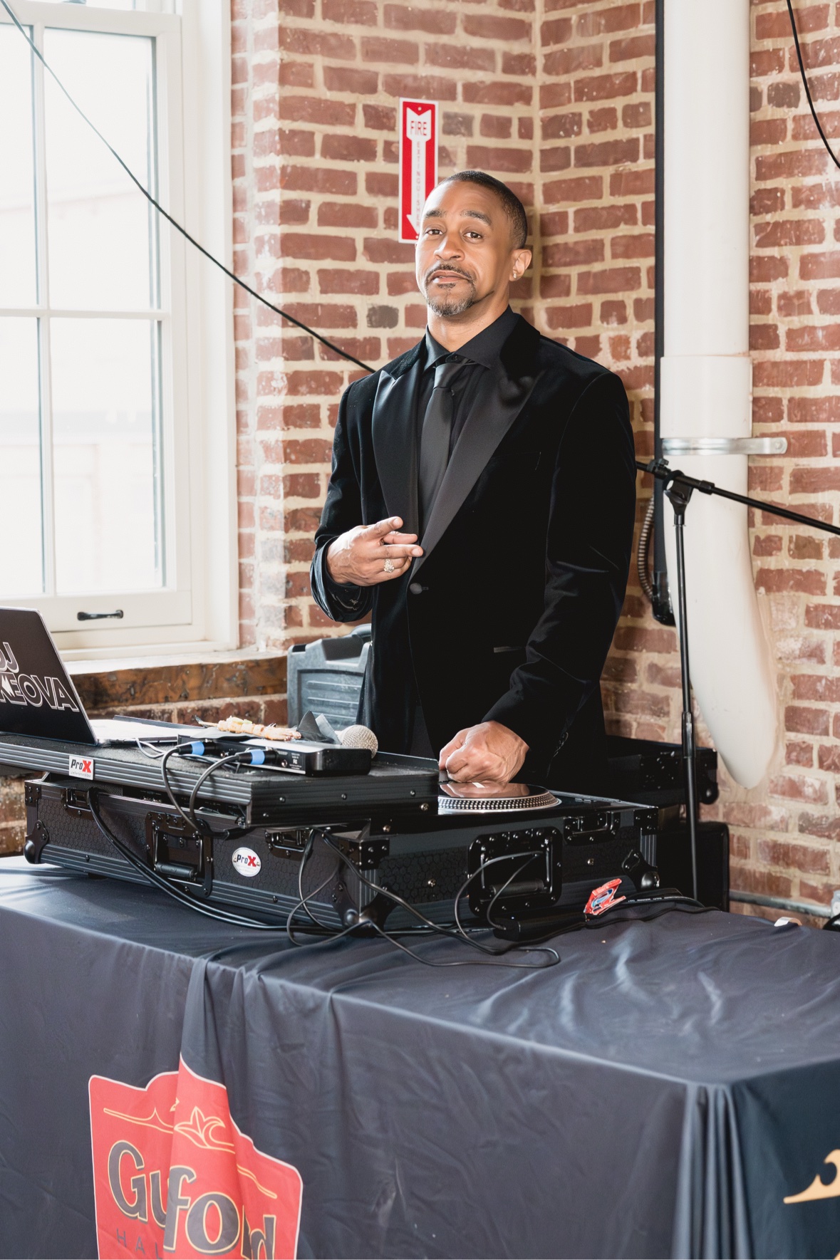 DJ Takeova in a black suit behind the decks at a formal corporate event