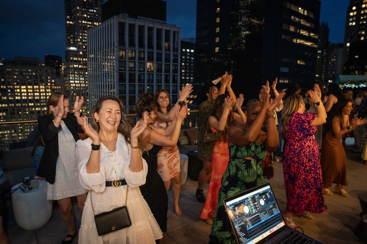 Guests dancing at a rooftop party with the DJ laptop visible