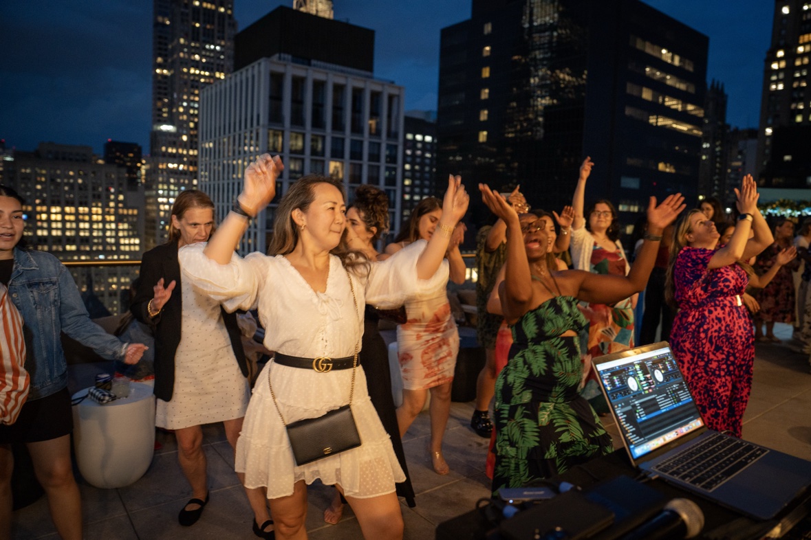 Guests dancing with hands up at a rooftop party with the NYC skyline behind them