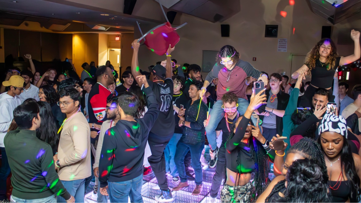 A packed young crowd dancing beneath colorful event lighting